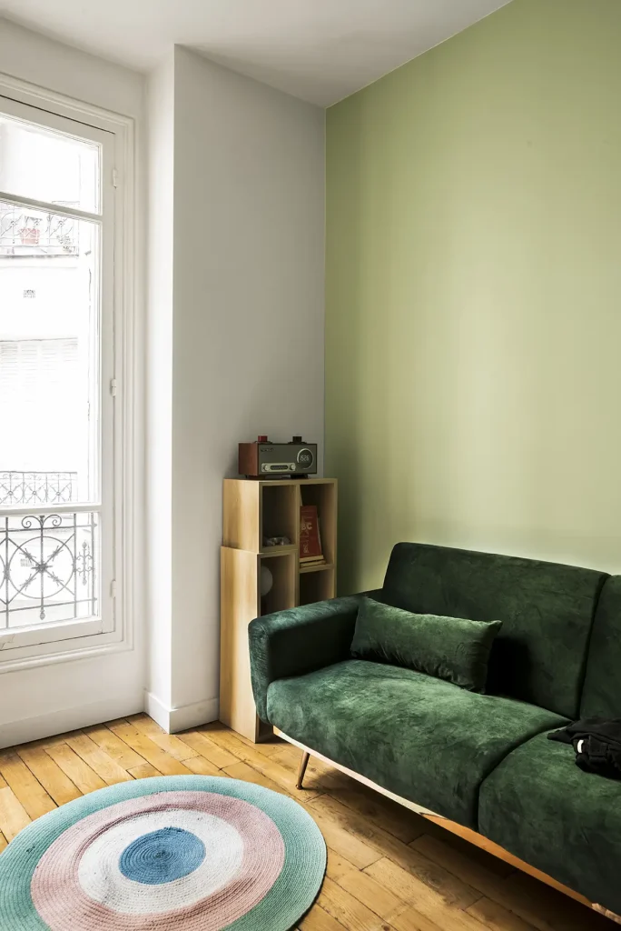 Salon d'appartement avec un canapé vert et un tapis rond.